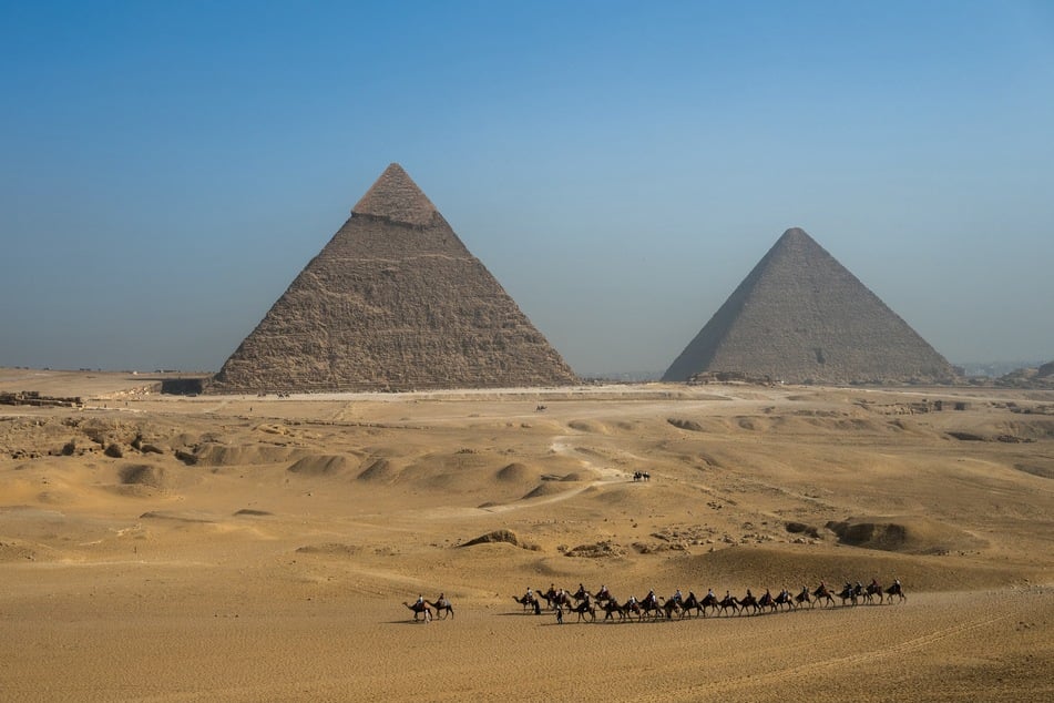 Tourists ride camels past the Great Pyramid of Khufu (Cheops, R) and the Pyramid of Khafre (Chephren, L) at the Giza Pyramids Necropolis on the outskirts of Giza on May 3, 2024.