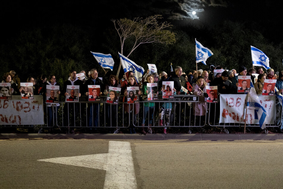 Protesters lift national flags and portraits of Israelis held hostage by Palestinian Hamas militants in Gaza since October 7, during a rally demanding their release outside Israeli Premier Benjamin Netanyahu's private residence in Caesarea north of Tel Aviv on January 27
