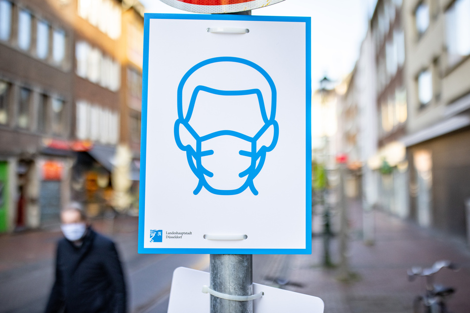 Düsseldorf: Ein Schild mit dem Symbol für Maskenpflicht ist an einem Straßenschild in der Innenstadt befestigt.