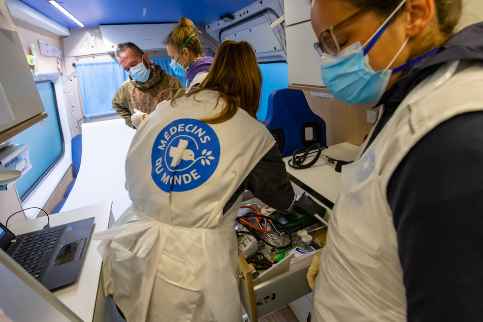 Eine Ärztin (2.v.l.) und zwei Assistentinnen behandeln einen Patienten in einem Behandlungsbus in München.