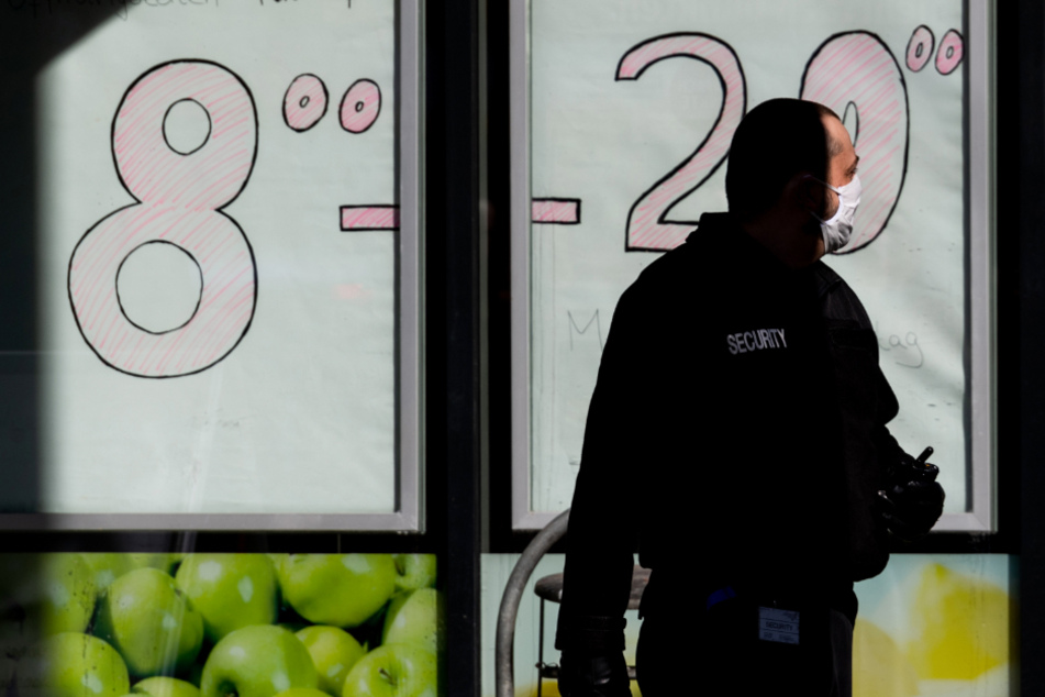Ein Sicherheitsmann steht vor einem Supermarkt und achtet auf den Einlass der Kunden. 