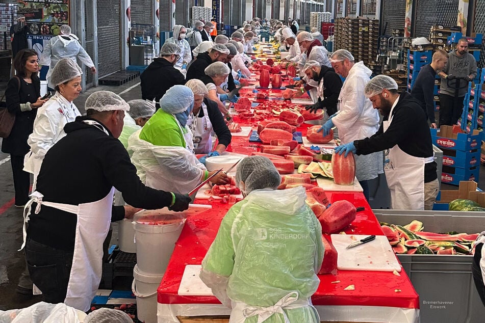 In einer Halle des Fruchthofs Berlin wird an einer langen Tafel Wassermelone geschnitten, was das Zeug hält.