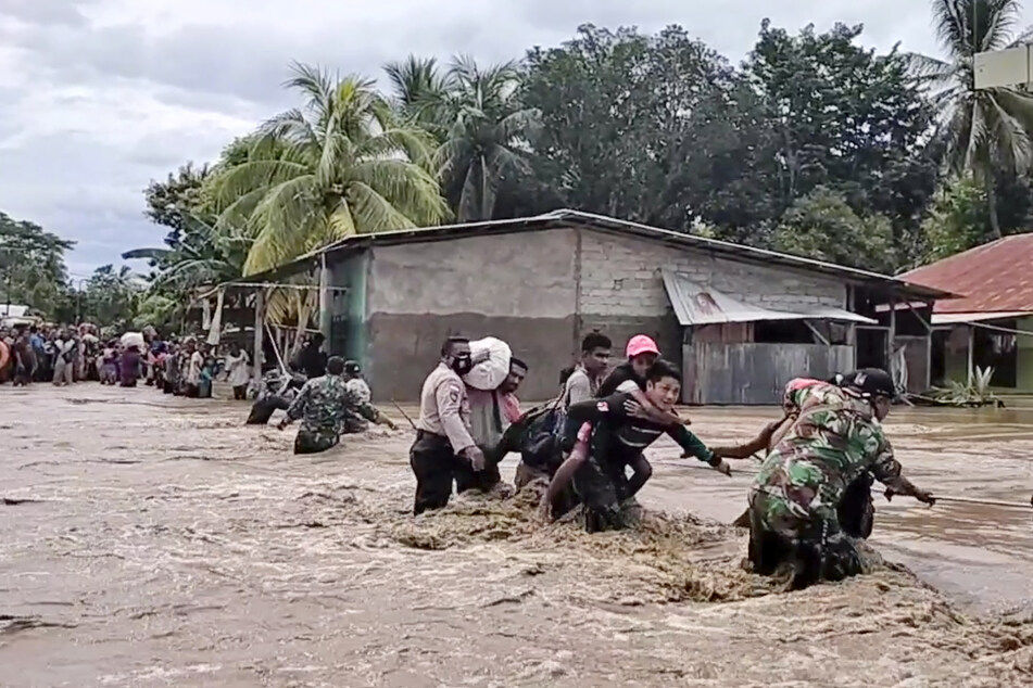 Soldaten und Polizisten helfen Anwohnern über eine überflutete Straße. Mindestens 18 Menschen sind durch eine Schlammlawine vom Vulkan Lewotolo auf der indonesischen Insel Lembata östlich von Bali getötet worden.