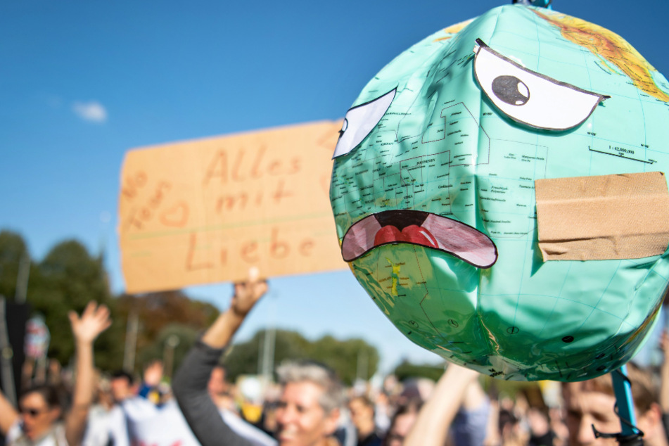 "Fridays for Future"-Demonstranten halten einen Luftballon mit Globusaufdruck hoch, der mit einem Pflaster und unglücklichen Gesichtszügen beklebt ist. (Archivbild)