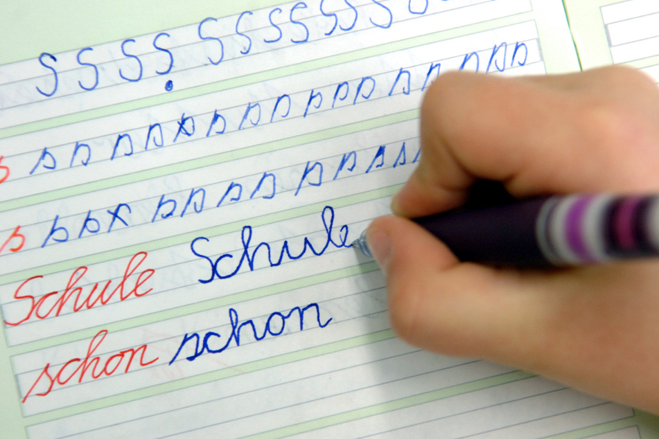 In einer Dorfschule schreibt ein Mädchen im Unterricht das Wort "Schule" in ihr Heft.