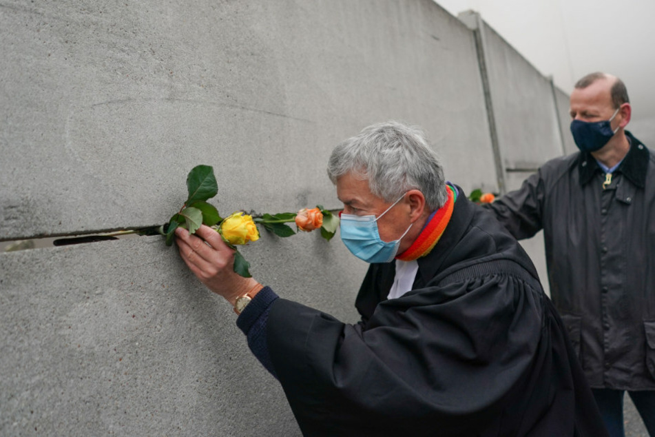 Thomas Jeutner (l.), Pfarrer der Evangelischen Versöhnungsgemeinde, und Axel Klausmeier, Direktor der Stiftung Berliner Mauer, stecken anlässlich des Mauerfalls vor 31 Jahren Rosen in die Hinterlandmauer.