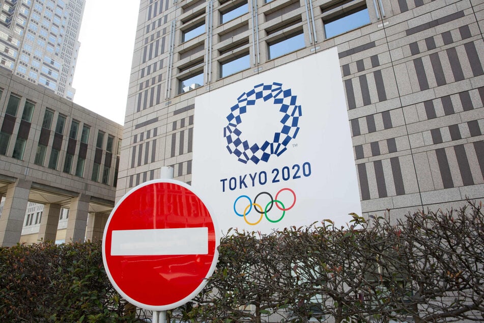 Verkehrsschild mit Verbot der Einfahrt steht vor dem Gebäude der Stadtregierung von Tokio, während im Hintergrund ein Banner mit dem Logo der Olympischen Spiele 2020 in Tokio zu sehen ist.