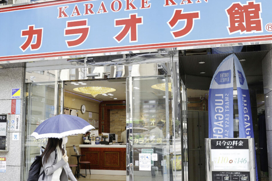 Japan, Tokio: Eine Passantin mit Mundschutz geht an einer wiedereröffneten Karaoke-Lounge vorbei.