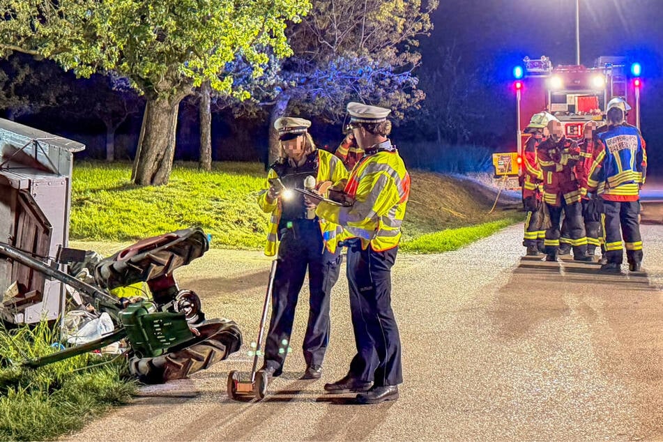 Einsatzkräfte von Polizei und Feuerwehr stehen neben dem umgestürtzten Einachser mit Anhänger.