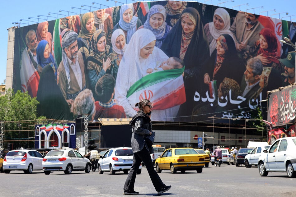 A woman crosses a street near a large political billboard along Enghelab Square in central Tehran, Iran, on May 26, 2026.