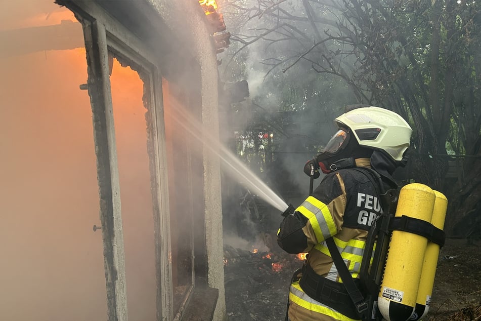 Feuerwehrkräfte näherten sich mit Atemschutz der bereits vollständig brennenden Laube.