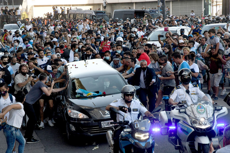 Der Leichenwagen mit den sterblichen Überresten von Diego Maradona verlässt das Regierungsgebäude begleitet von Fans.