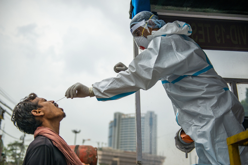 Ein Mitarbeiter des Gesundheitswesens (r) in Neu-Delhi nimmt bei einem Mann für einen Corona-Test einen Nasenabstrich.