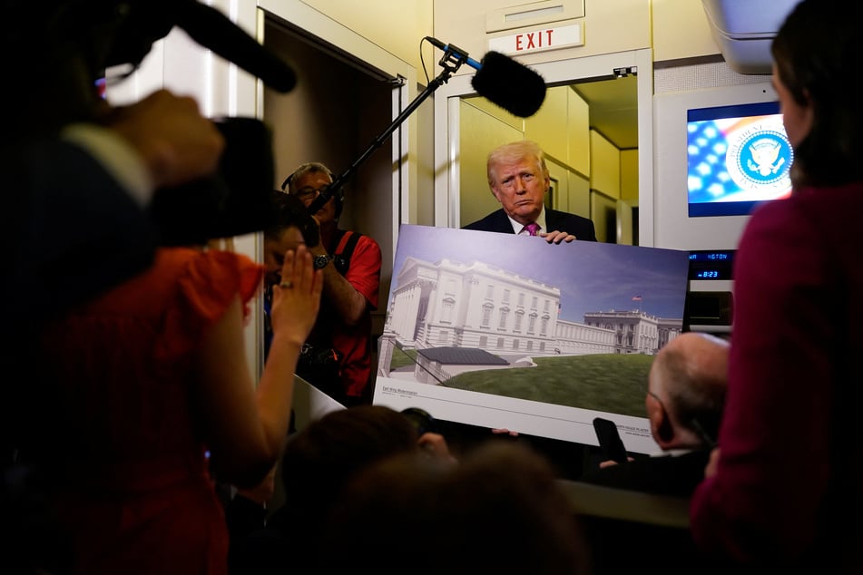 President Donald Trump talks to members of the media while holding up renderings of the planned White House ballroom, aboard Air Force One en route to Joint Base Andrews, on March 29, 2026.