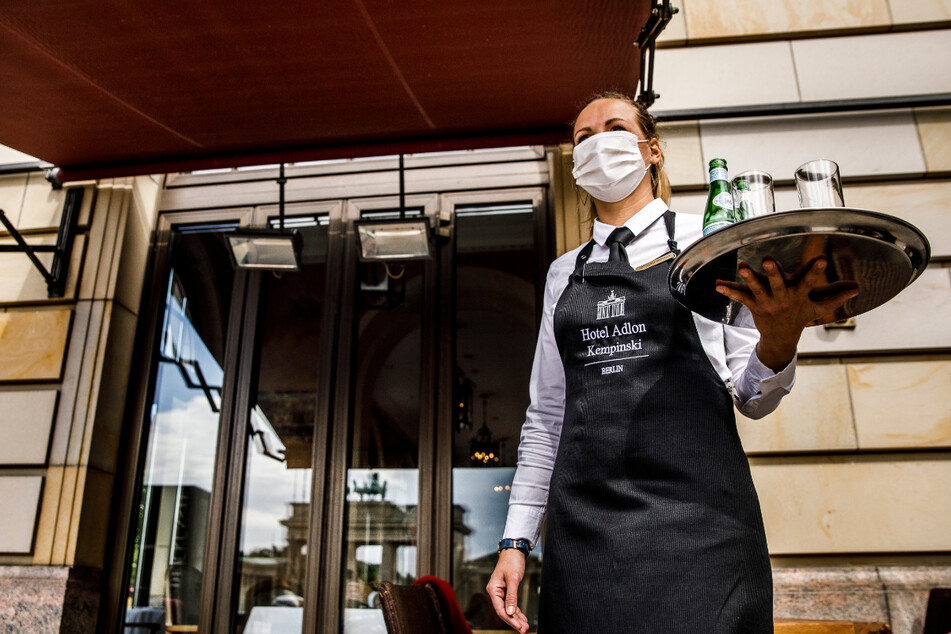 Auch das gehört zur "neuen Normalität": Eine Kellnerin mit einem Mund-Nasen-Schutz trägt ein Tablet mit Getränken auf der Terrasse des Hotels Adlon Kempinski am Pariser Platz in Berlin.