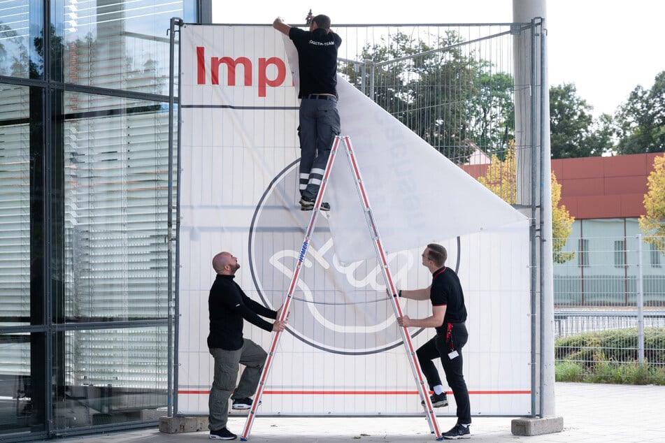 DRK-Logistiker entfernen vom Impfzentrum auf der Messe Dresden das große Transparent. Nach gut acht Monaten wird die Einrichtung nun geschlossen.