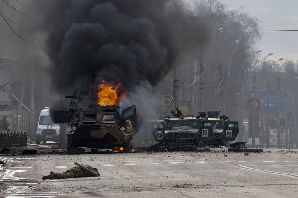 Ein gepanzerter Mannschaftswagen brennt nach Kämpfen am Sonntag in Charkiw auf einer Straße, während eine anscheinend leblose Person auf der Straße liegt.