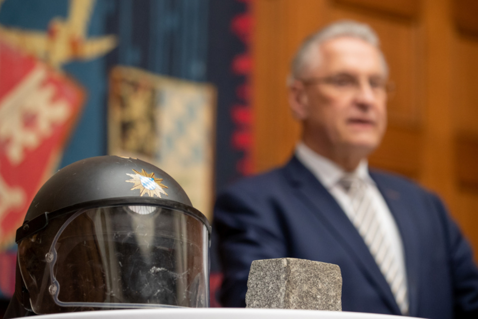 Joachim Herrmann (63, CSU), Innenminister von Bayern, steht hinter einem Polizeihelm, der beim G20-Gipfel 2017 in Hamburg durch einen Pflasterstein beschädigt wurde.