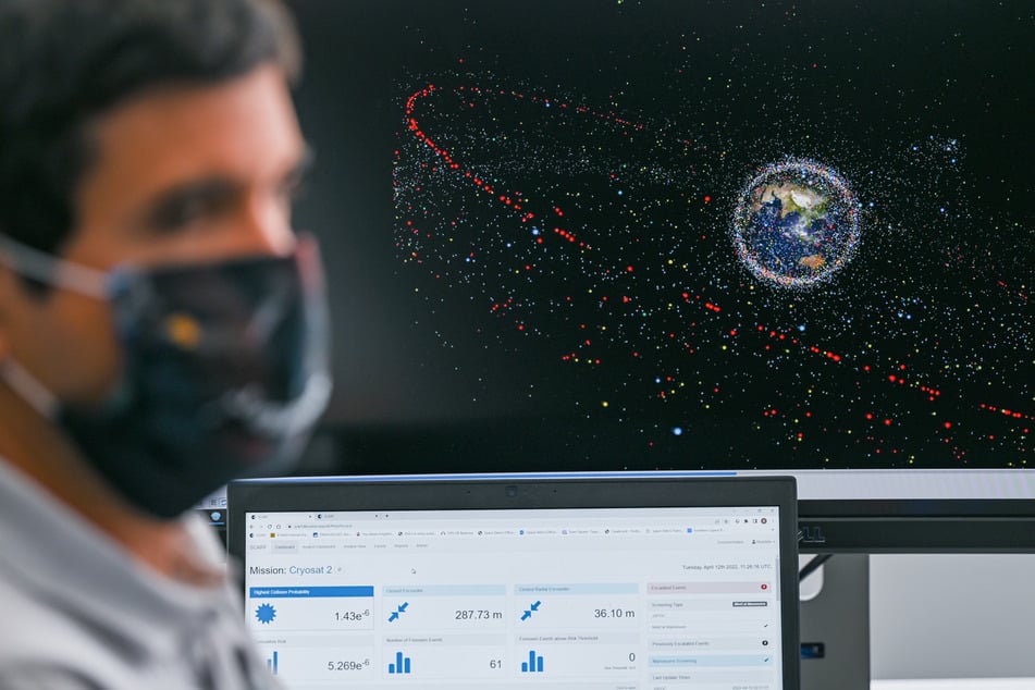 La ilustración detrás del ingeniero muestra la representación de los desechos espaciales en la órbita terrestre. Cuantos más haya, mayor será también el peligro que representan.