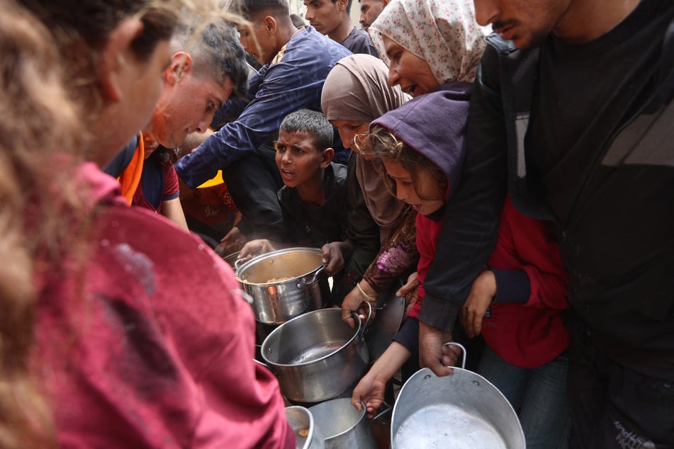 Palestinians wait to get a ration of hot food from a charity kitchen set up at the Islamic University campus in Gaza City on May 12, 2025.