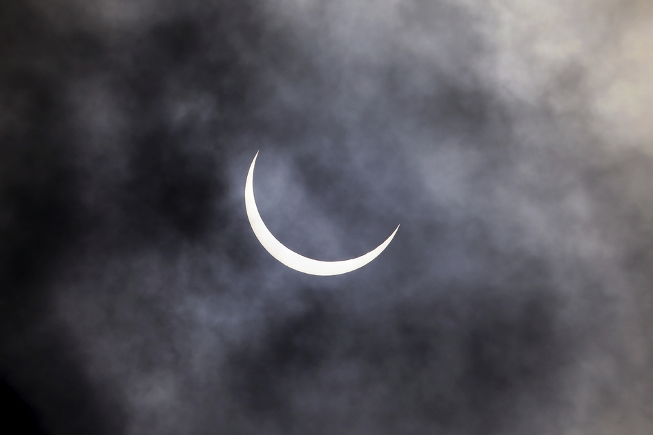 Indien, Neu Delhi: Die Sonnenfinsternis ist in Neu Delhi durch Wolken hindurch zu beobachten.