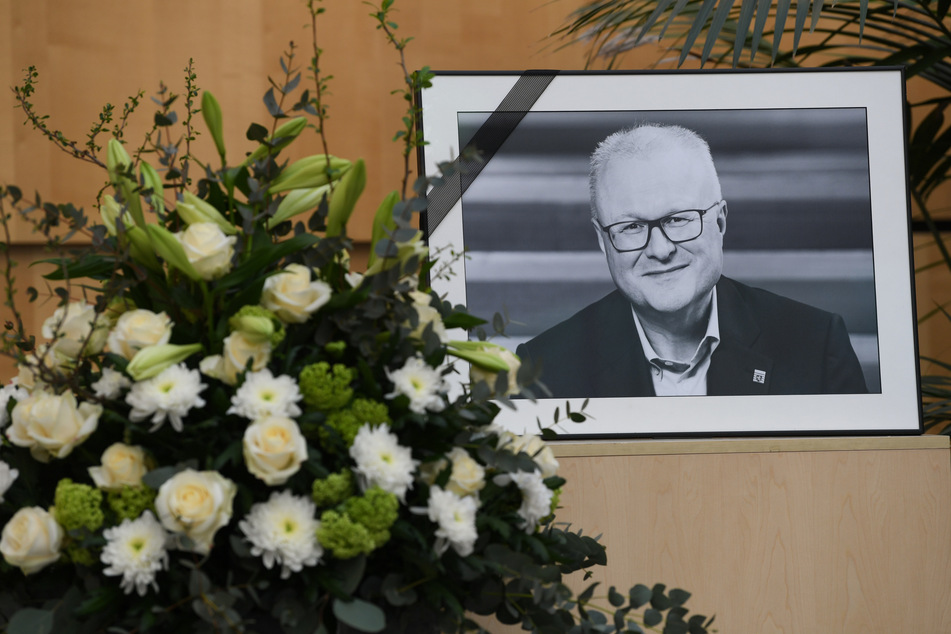 Ein Foto des hessischen Finanzministers Thomas Schäfer mit Trauerflor steht im Hessischen Finanzministerium auf einem Podest neben einem Blumengebinde.