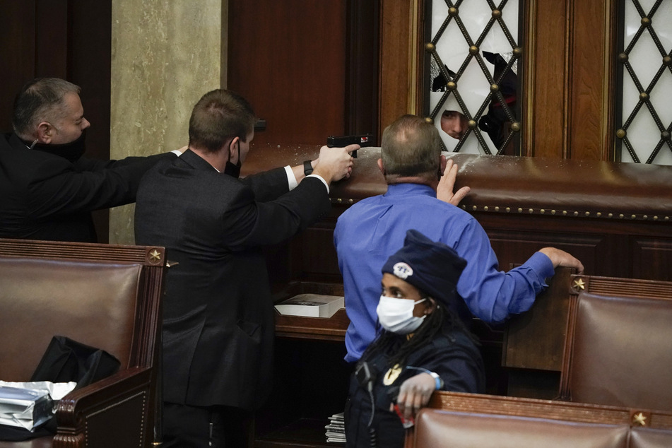 Szenen wie aus einem schlechten Film: Um Abgeordnete des Repräsentantenhauses zu schützen, richten Sicherheitsleute ihre Waffen auf Protestler, die durch eine eingeschlagene Scheibe in den Saal hineinschauen.