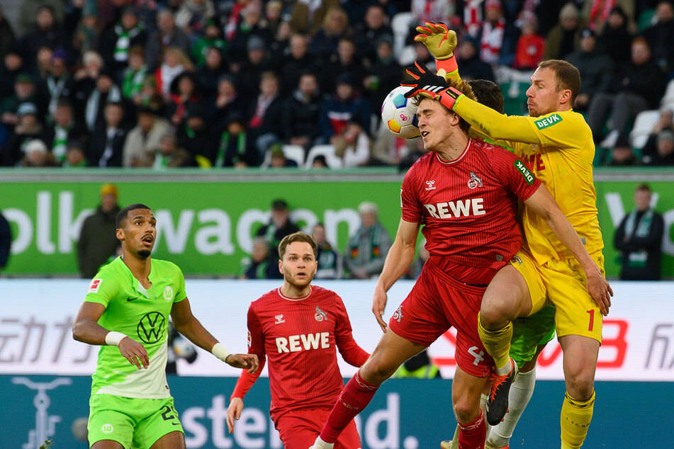 Kölns Torwart Marvin Schwäbe (r.) und Kölns Timo Hübers kämpfen mit Wolfsburgs Jonas Wind (verdeckt) um den Ball.