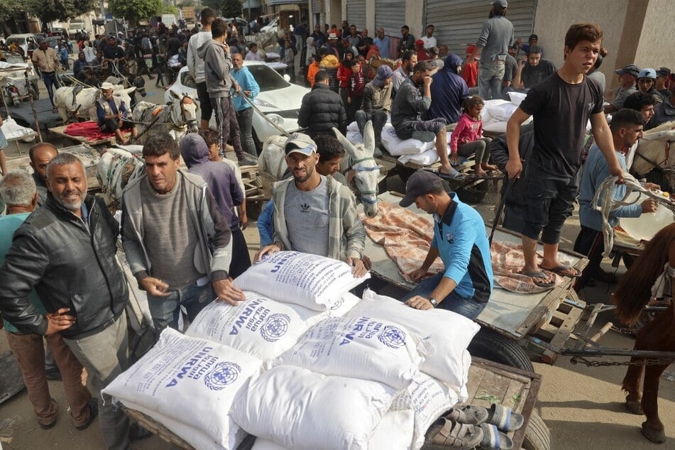 Palestinian people load their carts with sacks of flour at an UNRWA aid distribution center in Deir el-Balah in the central Gaza Strip.