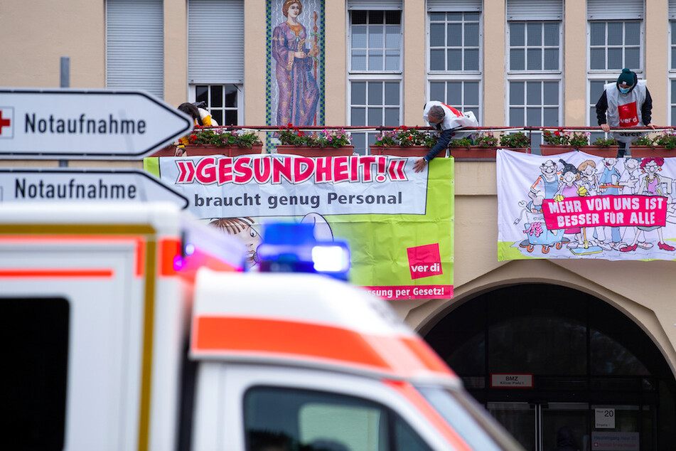 Krankenhaus-Mitarbeiter befestigen am Klinikum Schwabing während eines Warnstreiks Plakate mit der Aufschrift "Gesundheit braucht genug Personal" und "Mehr von uns ist besser für Alle".