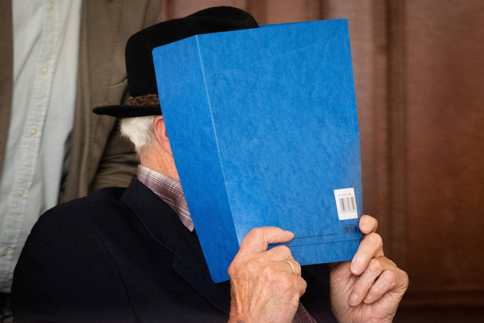 Der 93 Jahre alte Angeklagte versteckt sein Gesicht hinter einer Mappe.