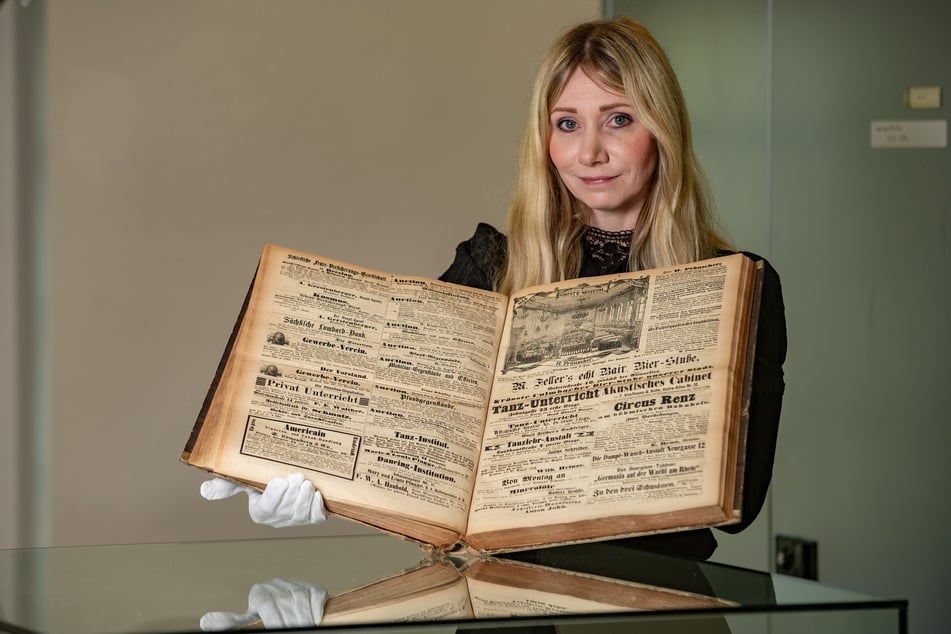 Dr. Sylvia Drebinger-Pieper (40) hält einen Sammelband des Dresdner Anzeigers in den Händen. Ab 1868 schaltete Hermann Präuscher hier immer wieder Werbeanzeigen.