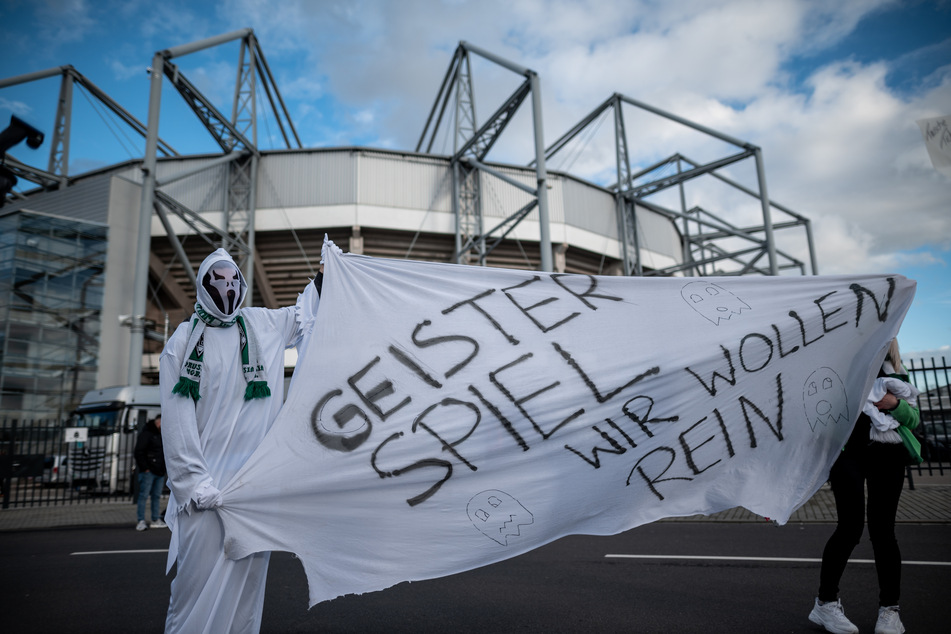 Fans in Geisterkostümen stehen am 11. März vor dem Stadion in Mönchengladbach mit einem Banner auf dem "Geisterspiel Wir wollen rein" steht.