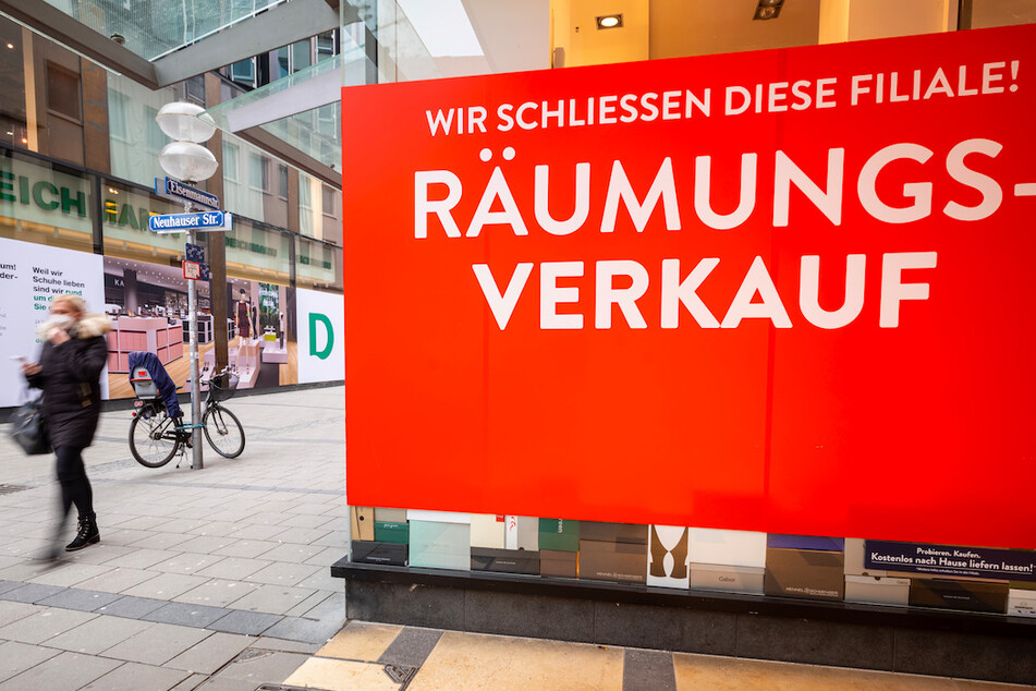 Ein Passantin läuft durch die fast leere Innenstadt an einem Geschäft vorbei, an dem das ein Schild mit der Aufschrift "Wir schliessen diese Filiale! - Räumungsverkauf" im Schaufenster klebt.