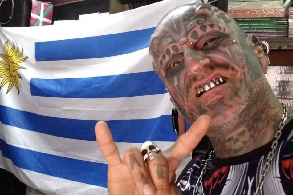 Victor Hugo Peralta Rodriguez flaunts his metal teeth in front of a Uruguayan flag.