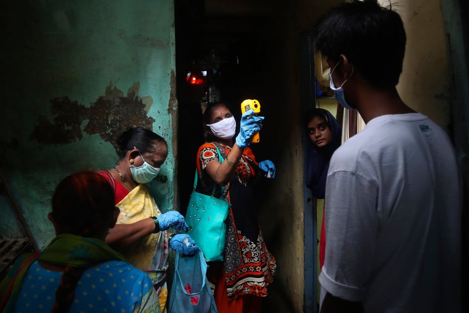 Eine Mitarbeiterin des Gesundheitswesens misst die Körpertemperatur von Bewohnern eines Slums.