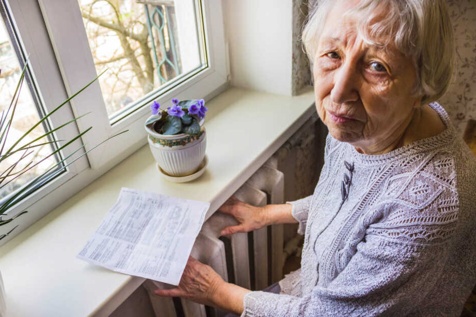 Eine Seniorin sitzt an ihrer Heizung blickt auf die Heizkosten-Abrechnung.