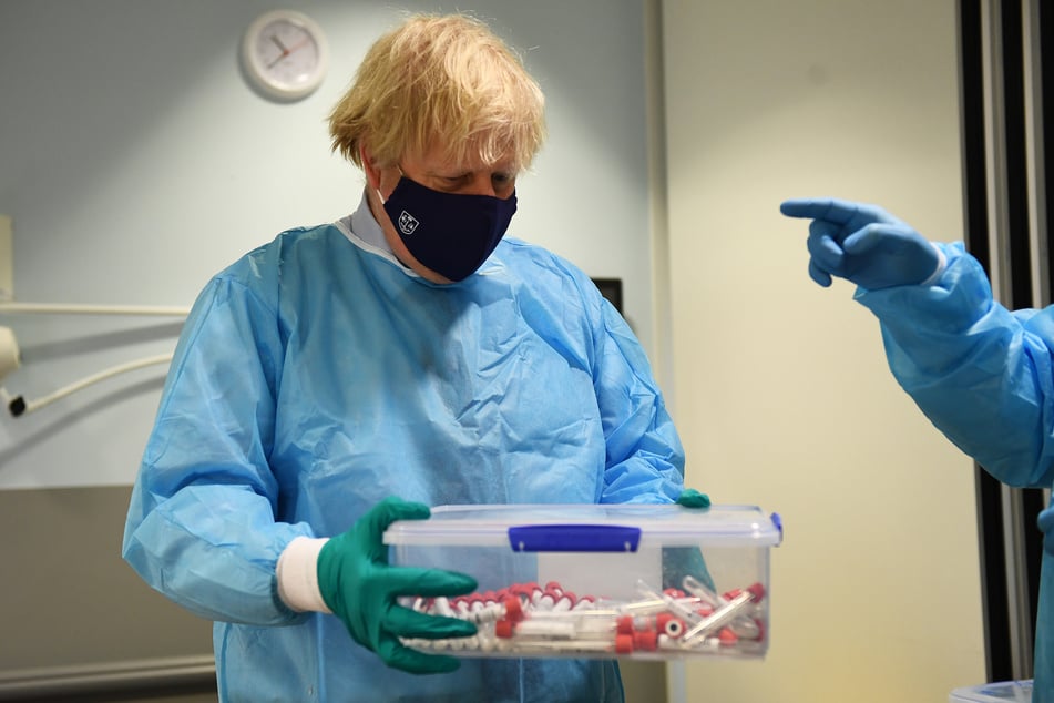 Glasgow: Boris Johnson (56), Premierminister von Großbritannien, hält Corona-Test-Proben in einem Plastikgefäß. Die britische Regierung rechnet weiterhin mit Impfstoff-Lieferungen.