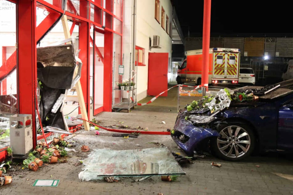 Nach dem Unfall steht der stark beschädigte Tesla vor den Trümmern der Fassade des Baumarktes in Nortorf.