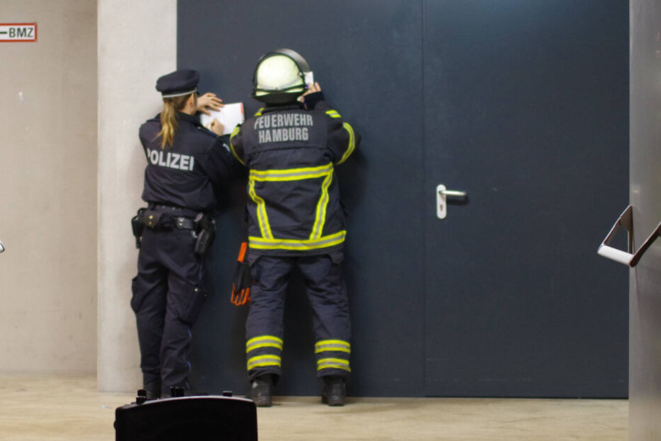 Eine Polizisten und ein Feuerwehrmann machen an einer Tür Notizen.