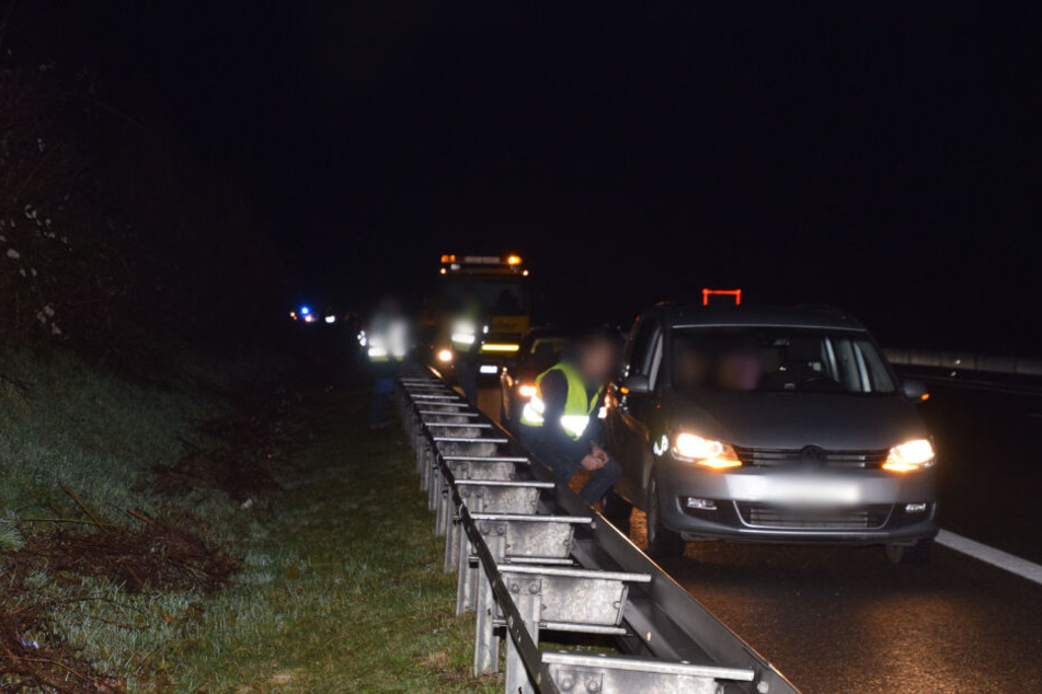 Ein Autofahrer sitzt neben seinem Wagen auf der Leitplanke.