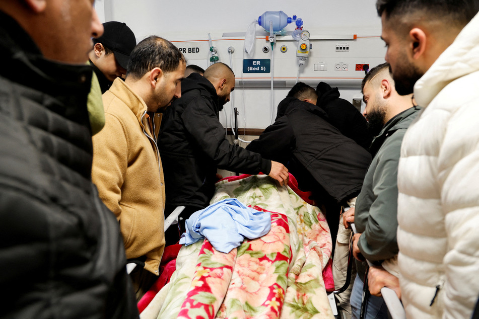 Palestinians gather around the bed of one of the men killed in the hospital attack.