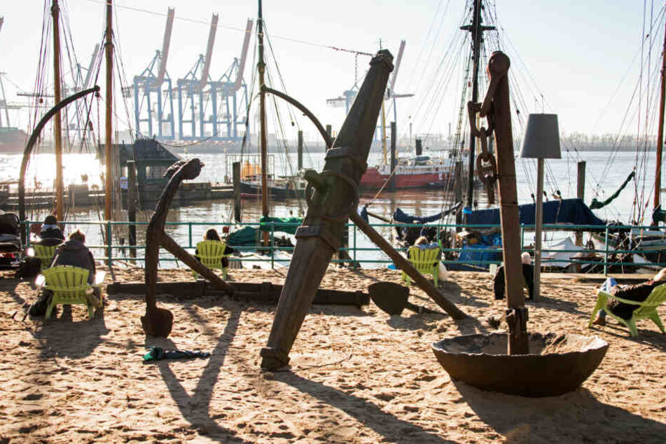 Auf Stühlen im Sand genießen Menschen die Sonne am Museumshafen Övelgönne.