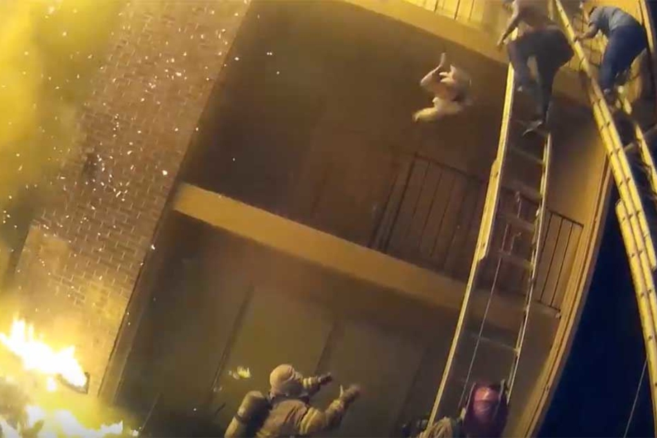 Das Kind wurde aus der 2. Etage geworfen. Unten steht der Feuerwehrmann bereit, es aufzufangen.