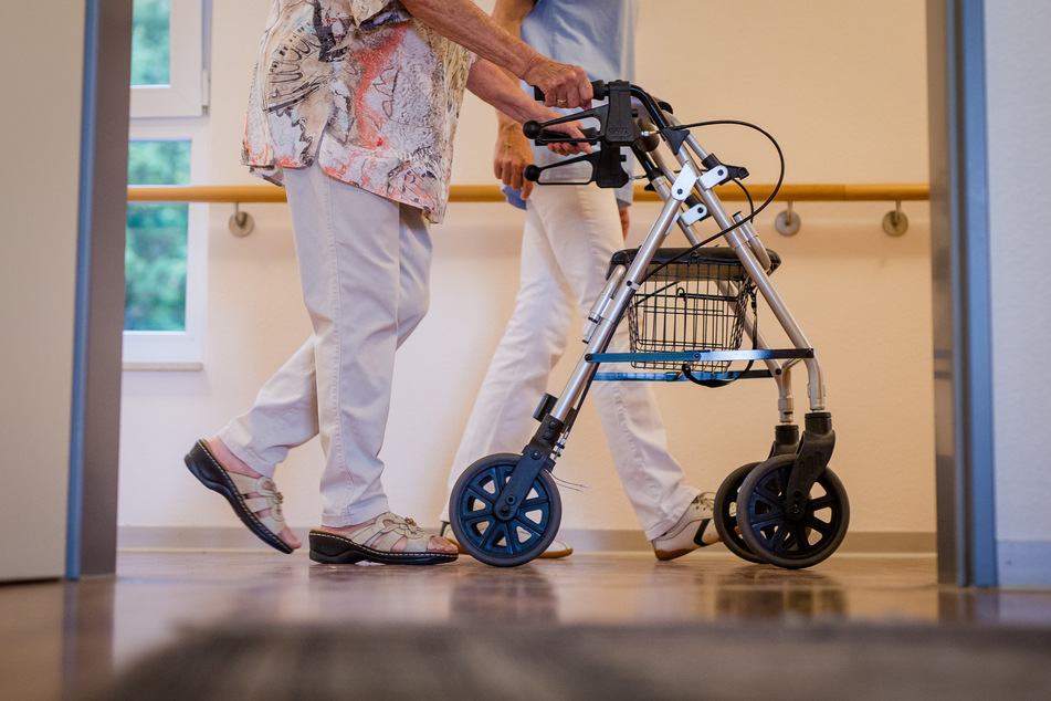 Eine Pflegekraft geht in einem Pflegeheim mit einer älteren Frau über einen Korridor.