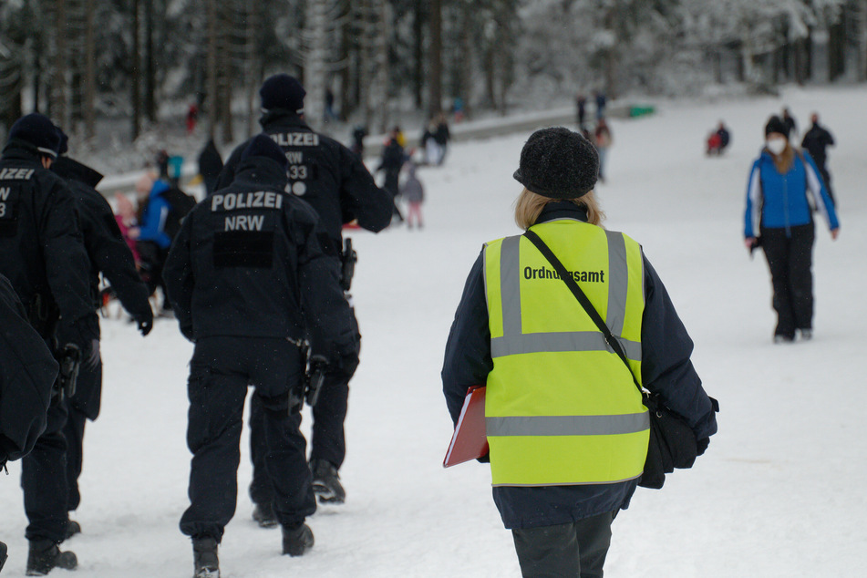 Polizisten und eine Mitarbeiterin des Ordnungsamtes stehen auf einer Piste im Skigebiet in Winterberg. Nach dem großen Andrang in den letzten Tagen sind die Pisten und Parkplätze nun gesperrt