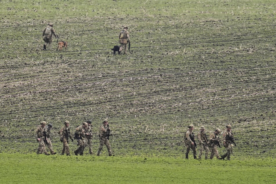 Behörden gehen über ein Feld in der Nähe eines Fahrzeugs, das in Zusammenhang zu dem Verdächtigen nach tödlichen Schüssen auf eine Politikerin und ihren Ehemann stehen soll.