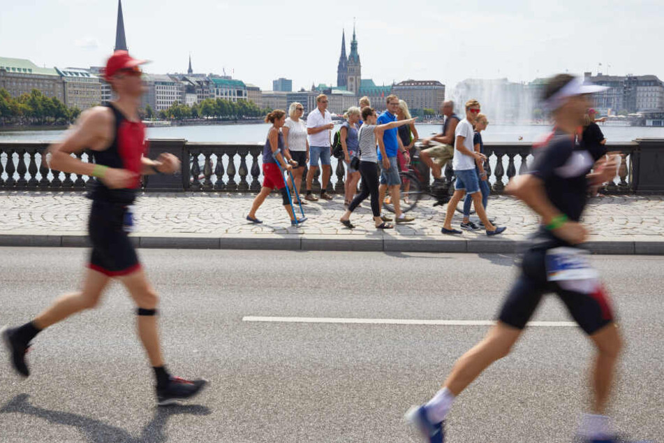Triathleten laufen über die Lombardsbrücke. Im Hintergrund sind die Binnenalster und das Rathaus zu sehen.