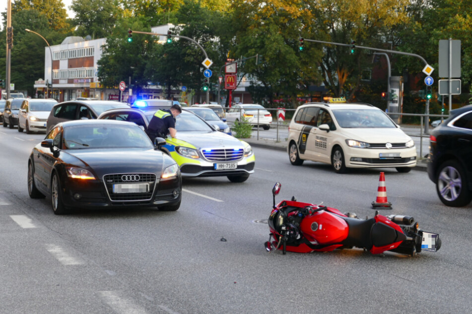 Nach dem Unfall liegt das beschädigte Motorrad auf der Straße, ein Polizist sichert den Unfallort.