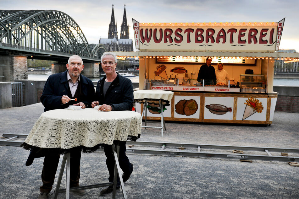 Die Tatort Kommissare Max Ballauf (r, Klaus J. Behrendt) und Freddy Schenk (l, Dietmar Bär) stehen in Köln vor Dreharbeiten an der Wurstbraterei vor dem Dom (Archivbild).